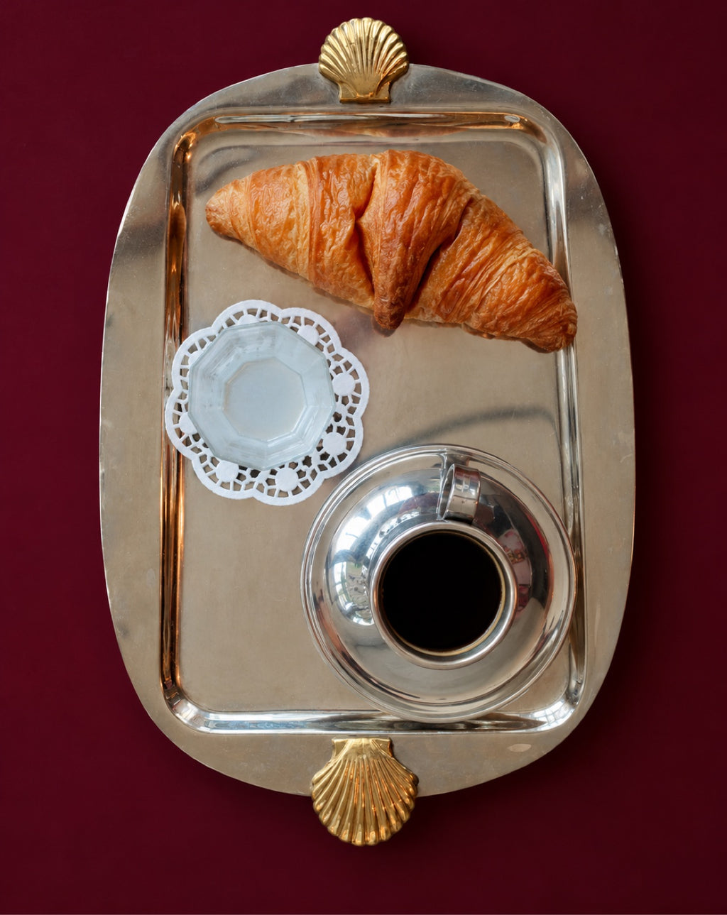 Silver serving tray with croissant and coffee on burgundy